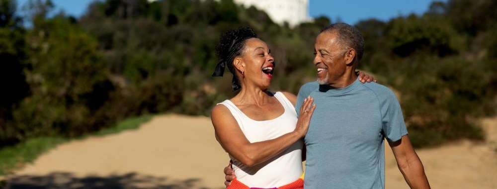 two senior citizens walking along side a beach laughing