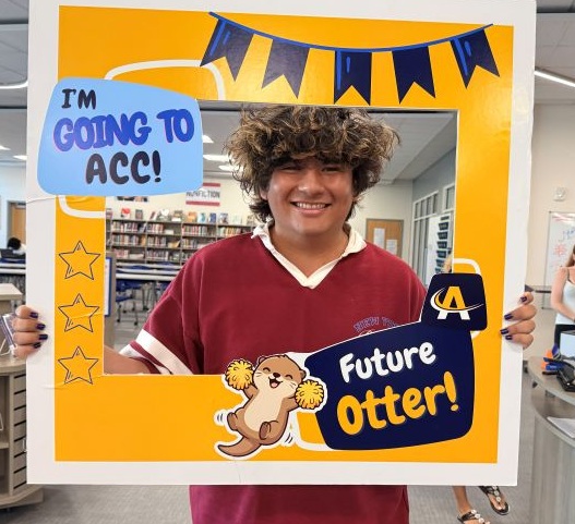 Student smiling and holding a photo frame sign that reads 'I’m going to ACC! Future Otter!' inside a library setting.
