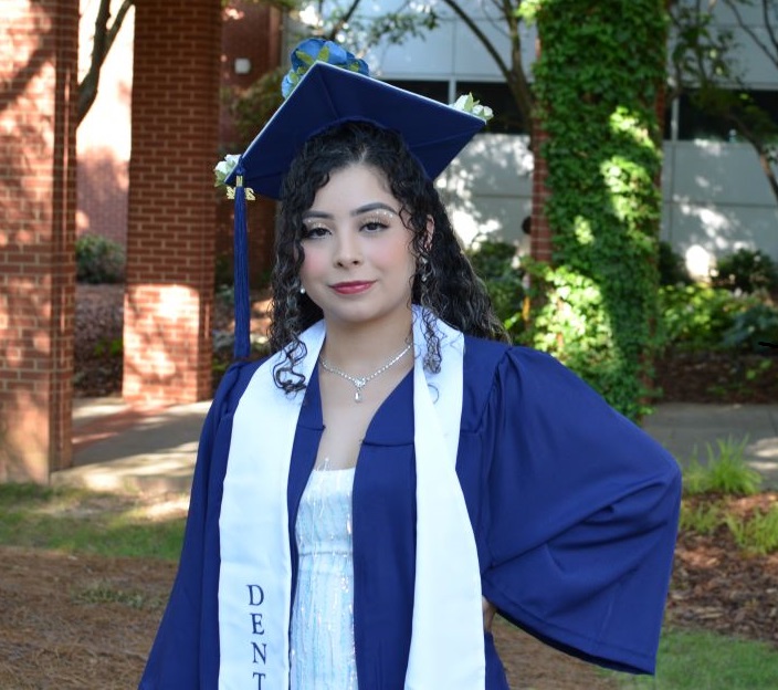 female acc graduate standing out of auditorium in her blue acc graduation regalia posing for camera