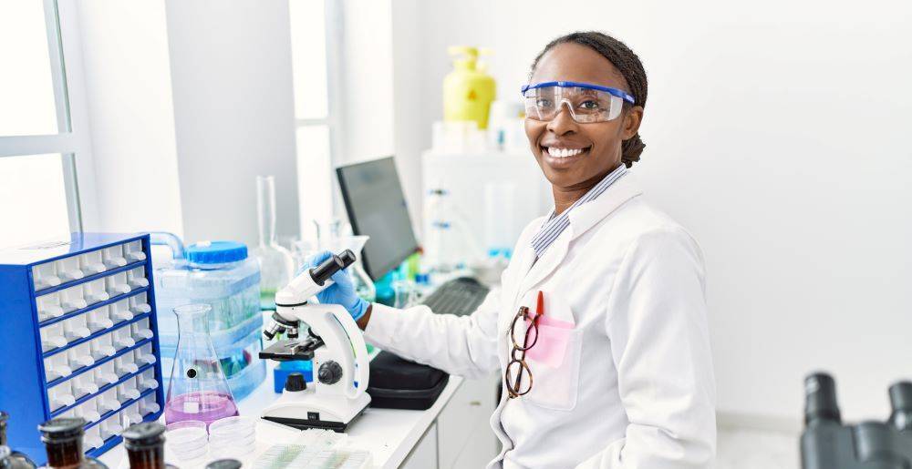 African woman working at scientist laboratory looking positive  and smiling with a confident smile