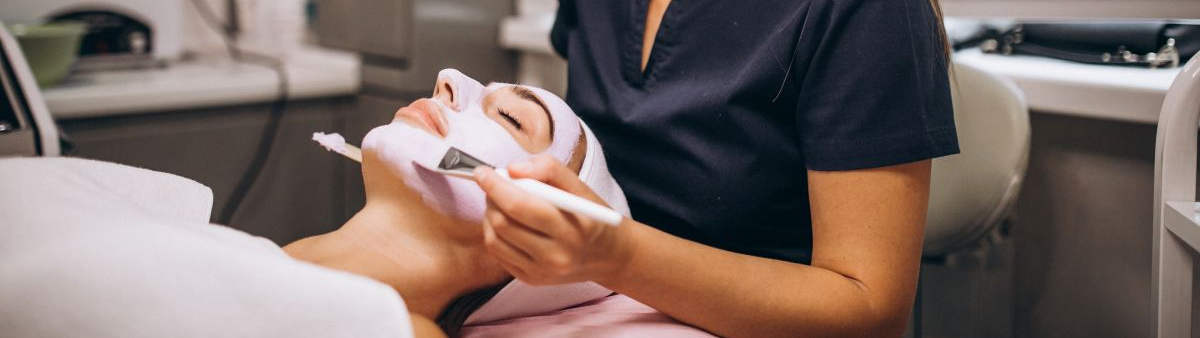 Cosmetology student applying a facial mask to a client at a beauty salon, demonstrating skincare techniques in a hands-on learning environment.