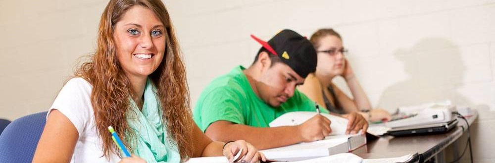 young female student sitting at desk smiling at the camera